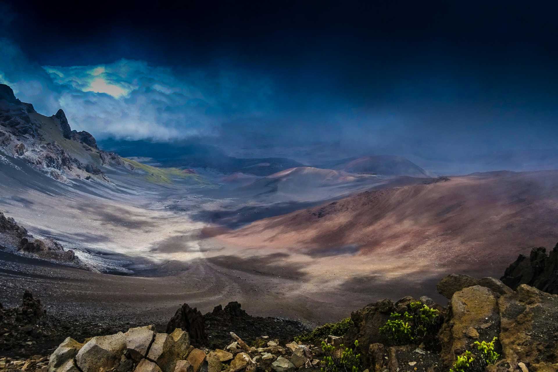 A breathtaking view of Haleakalā Crater in Maui, Hawaii, taken at dusk with dramatic clouds and rocky terrain.